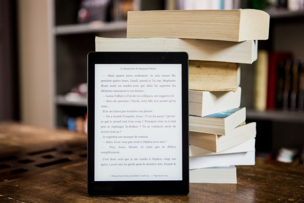e-reader with a stack of books behind it