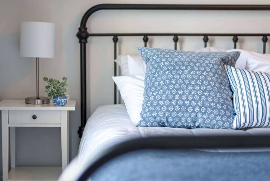 cozy bed with simple nightstand with lamp and plant